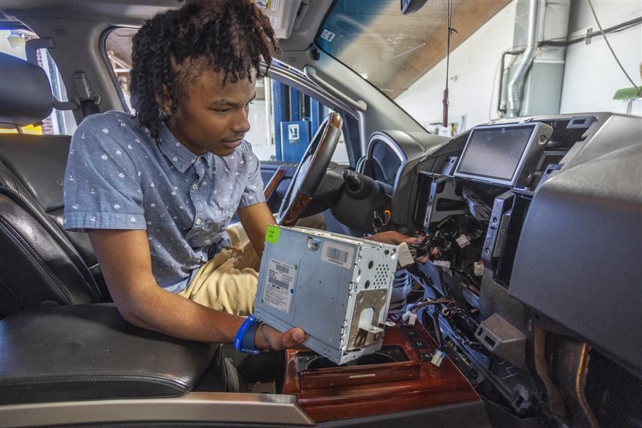 A student works to repair a radio in a car.